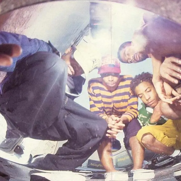 Fisheye lens group portrait of young men in 90s hip-hop style posing closely together on the ground