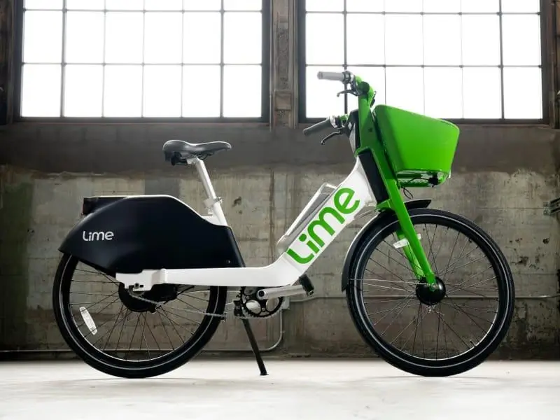 Studio view of a Lime electric bike showcasing its low step-through frame, smaller wheels, front basket, and rear-mounted battery design for accessible urban mobility