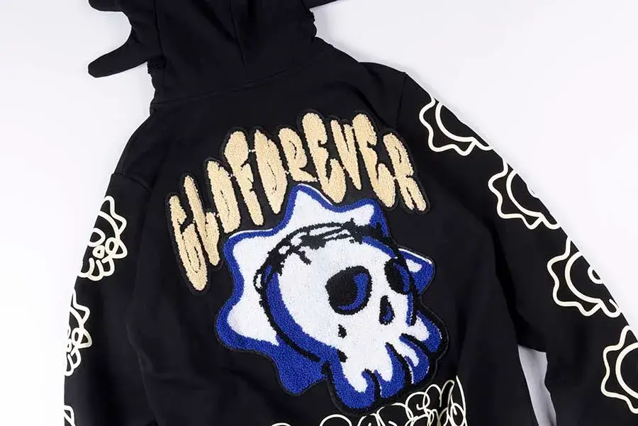 Black Glo Gang Glo Man full zip hoodie featuring a large chenille “GLOGANG” back graphic with a stylized skull motif in blue and white, sculpted character hood with spiked detailing, and sleeve graphics on a clean studio background