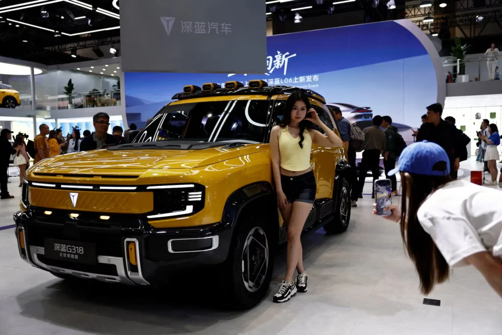Yellow Deepal G318 electric SUV displayed at Auto China 2026, with a model posing beside the vehicle as attendees photograph it, showcasing rugged design elements, roof-mounted lights, and a busy exhibition booth environment