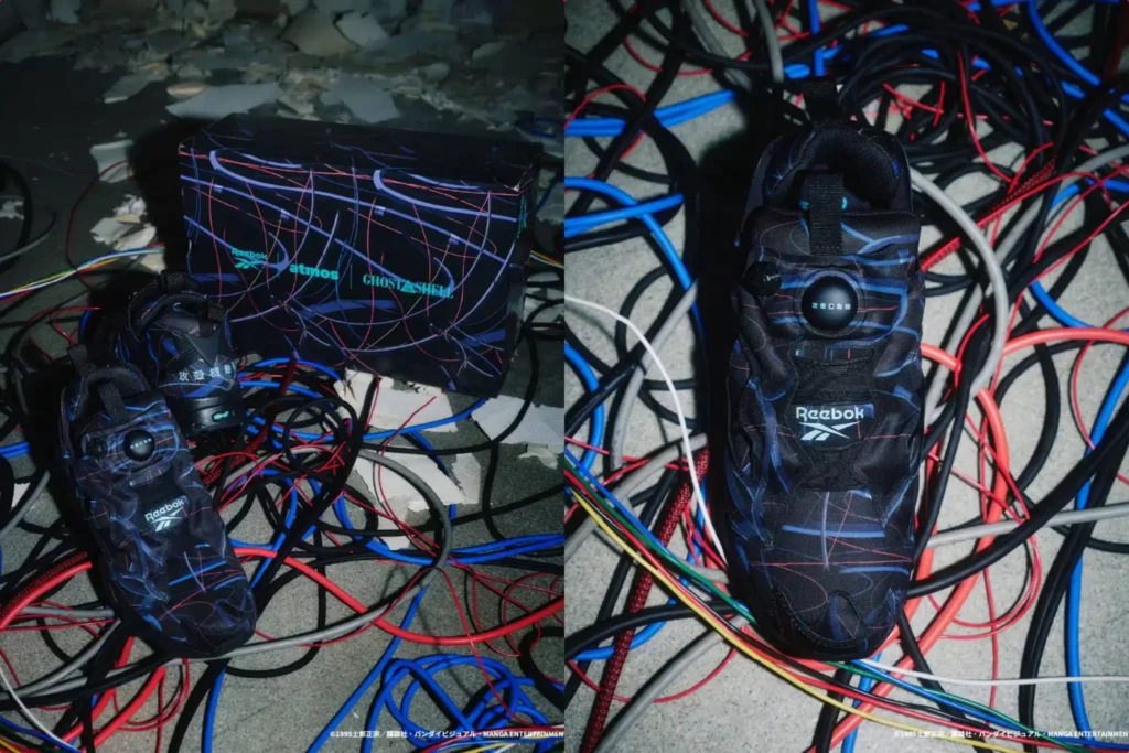 A pair of futuristic black sneakers with neon blue and red abstract line graphics are displayed among a chaotic spread of tangled cables on a concrete floor. One image shows the shoes beside a matching shoebox branded with Reebok, atmos, and Ghost in the Shell, while the other highlights a top-down view of the shoe, featuring a central circular detail near the tongue, a pull tab, and visible Reebok branding. The cyberpunk aesthetic is reinforced by the surrounding wires and dim, industrial setting