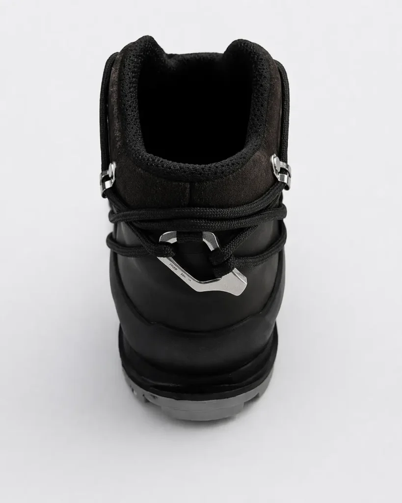 Close-up rear view of a black hiking boot showing textured suede collar, wraparound cord lacing secured with angular metal hardware, and a durable molded heel with rugged outsole