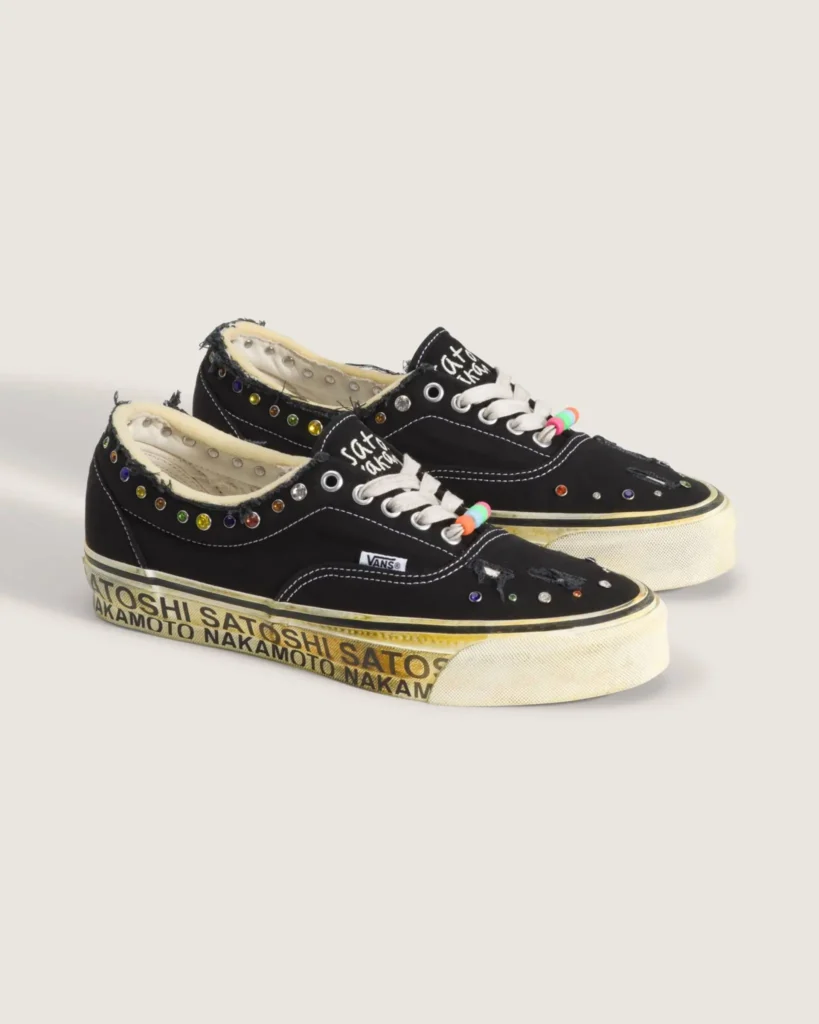 Pair of black Vans Era 95 shoe featuring distressed canvas uppers with frayed edges, multicolor gemstone embellishments along the collar and toe, white laces with colorful bead accents, exposed inner lining, and a yellowed midsole printed repeatedly with “Satoshi Nakamoto” branding