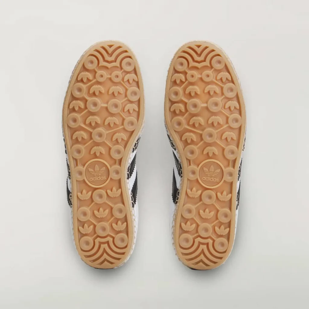 bottom view of adidas Samba shoe featuring gum rubber outsoles with circular traction pods, trefoil logos, and geometric grip patterns in a symmetrical layout