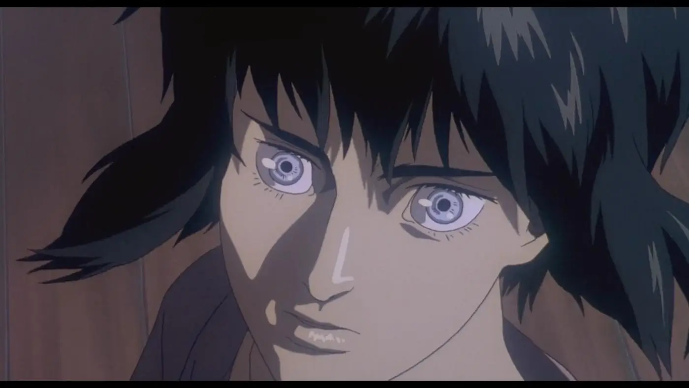 Close-up anime still of a female character with short black hair and pale skin, gazing intensely forward with wide, reflective eyes. Soft, muted lighting casts gentle shadows across her face, emphasizing a serious, contemplative expression, while the blurred background suggests an interior setting