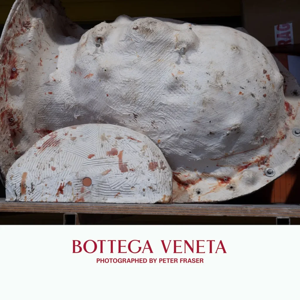 White sculptural mold resembling a human torso with visible bolts and textured surface, marked by reddish stains, displayed on a workshop shelf; campaign text below reads “Bottega Veneta, Photographed by Peter Fraser.”