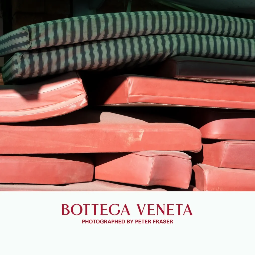 Stack of worn red seat cushions layered with striped padding on top, arranged in a dimly lit storage or workshop setting; campaign text below reads “Bottega Veneta, Photographed by Peter Fraser.”