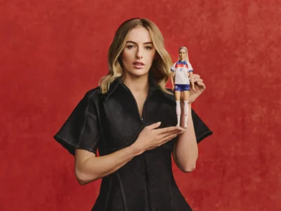 Chloe Kelly holding Barbie-style doll in England football kit against red background symbolizing athlete representation and identity