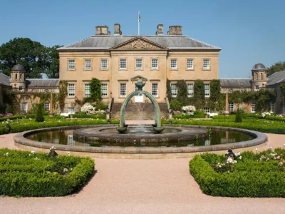 Dumfries House estate in Ayrshire, Scotland, featuring a symmetrical 18th-century mansion with ivy-clad stone wings, formal gardens, and a central fountain in the foreground