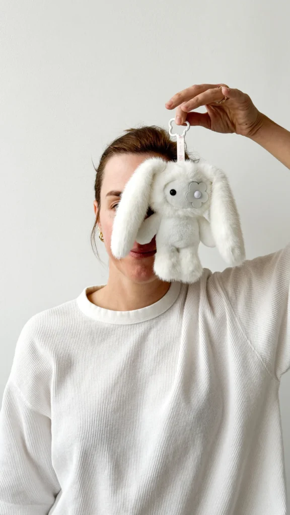 Cj Hendry holding a white juju plush keychain by Cj Hendry against a minimal backdrop, highlighting soft texture, character design, and collectible art toy scale