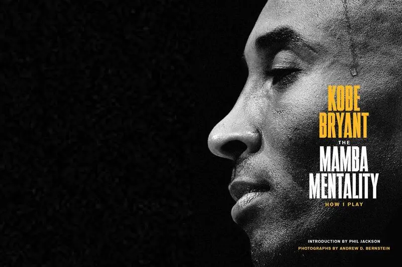 Black-and-white profile portrait of Kobe Bryant facing right, with a focused, contemplative expression and visible sweat along his temple. The right side of the image features bold typography reading “Kobe Bryant: The Mamba Mentality – How I Play,” set in yellow and white text against a dark background, emphasizing the iconic athlete and the book’s title