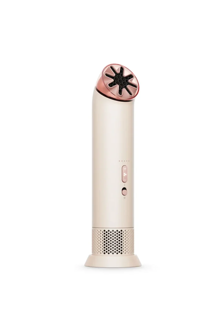 Compact handheld cooling device by Dyson in a soft beige and blush finish, featuring a precision star-shaped airflow nozzle, front-mounted control buttons, and a perforated base for air intake, representing the HushJet Mini Cool fan’s refined, portable design