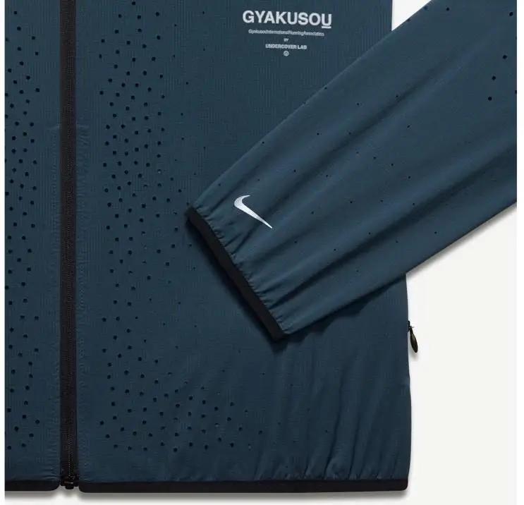 Close-up of a Nike Gyakusou technical jacket in deep teal, featuring laser-cut perforations for ventilation, a front zip closure, and a sleeve with a white Swoosh logo, highlighting performance-focused design details