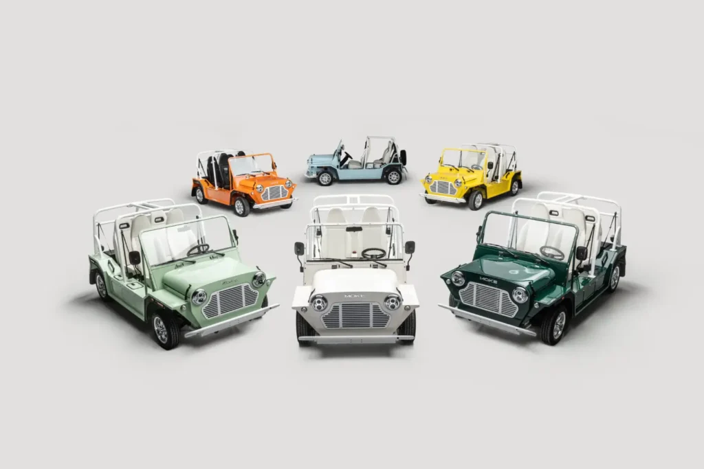 Group of MOKE GEN 1 EV vehicles in multiple colors arranged in a semi-circle, showcasing open-air electric design and classic compact proportions