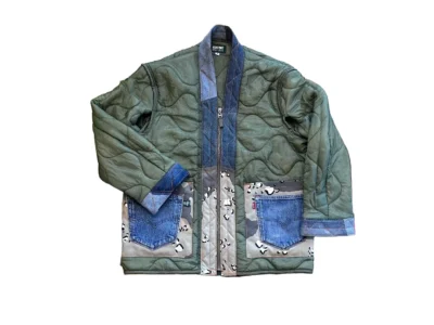 Front view of a green quilted jacket displayed on a plain background, featuring a wavy stitched pattern, denim trim along the collar and cuffs, and large patch pockets combining blue denim and patterned fabric