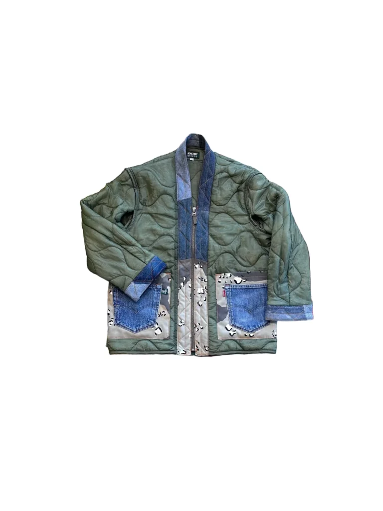 Front view of a green quilted jacket displayed on a plain background, featuring a wavy stitched pattern, denim trim along the collar and cuffs, and large patch pockets combining blue denim and patterned fabric