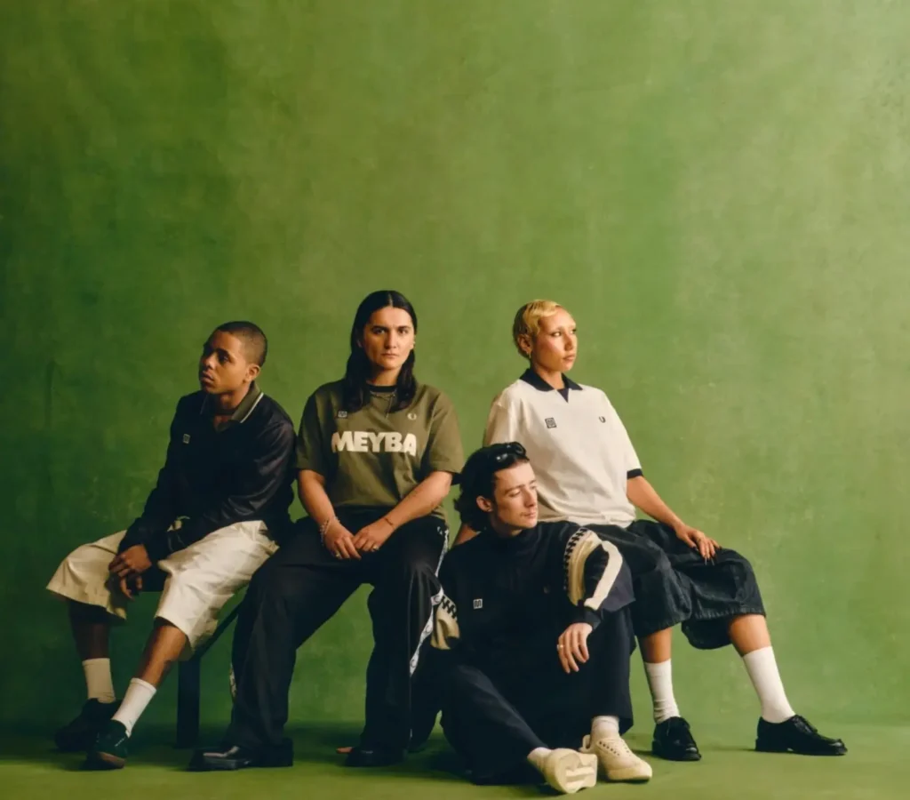 Four people seated and posed against a green backdrop, wearing casual sportswear with MEYBA branding