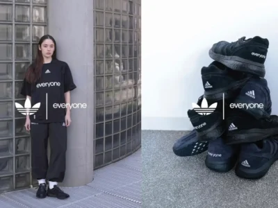 A split-image composition showcasing a minimalist Adidas “everyone” collaboration in both lifestyle and product form. On the left, a model stands against a curved glass-block wall and concrete column, wearing an oversized black Adidas T-shirt and loose black pants. The shirt features a small Adidas logo at the chest with the word “everyone” printed prominently across the front. The look is paired with black sneakers and white socks, emphasizing a relaxed, monochrome aesthetic. On the right, a stacked arrangement of black Adidas sneakers is displayed on a textured floor. Each pair features subtle Adidas branding alongside the word “everyone,” reinforcing the collaborative identity. Overlaid between both scenes are the Adidas trefoil logo and the word “everyone,” visually tying the two halves together into a cohesive campaign-style presentation