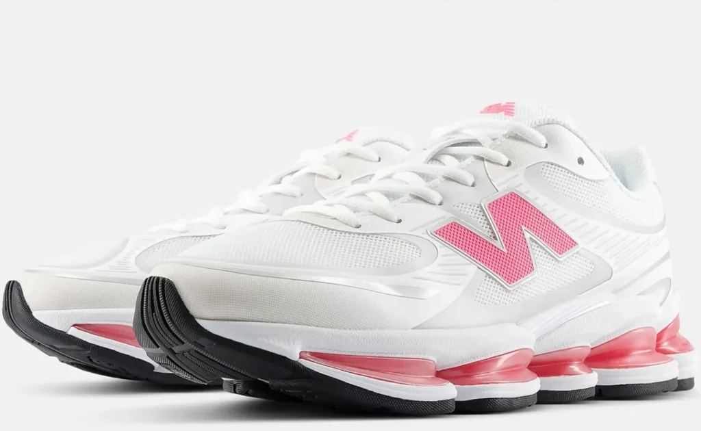 An angled front view of the New Balance sneakers, displaying the white mesh upper, pink logo accents, and layered sole construction with pink cushioning pods visible along the midsole