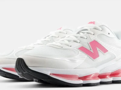 An angled front view of the New Balance sneakers, displaying the white mesh upper, pink logo accents, and layered sole construction with pink cushioning pods visible along the midsole
