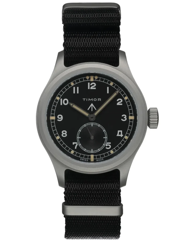 A clean studio shot of a brushed metal field watch with a black dial, luminous Arabic numerals, and a small seconds subdial, paired with a black fabric strap against a plain light background