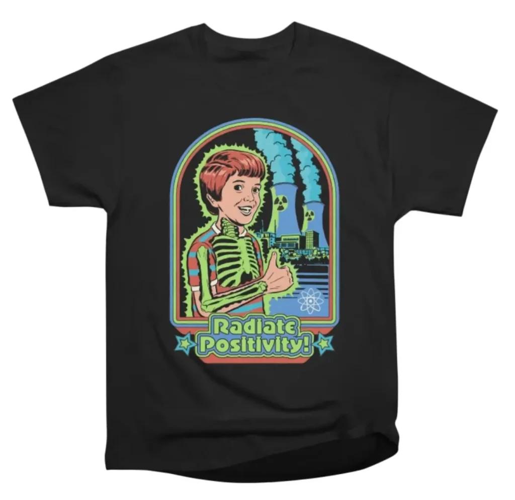 Steven Rhodes Radiate Positivity T-shirt – retro cartoon design with skeleton boy, nuclear plant, and 'Radiate Positivity!' text on a black tee
