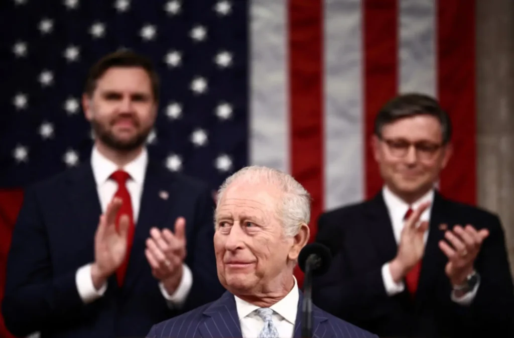 Mid-length view of King Charles III at the podium during his address to the U.S. Congress, with Vice President JD Vance (left) and Speaker Mike Johnson (right) clapping behind him in front of an American flag