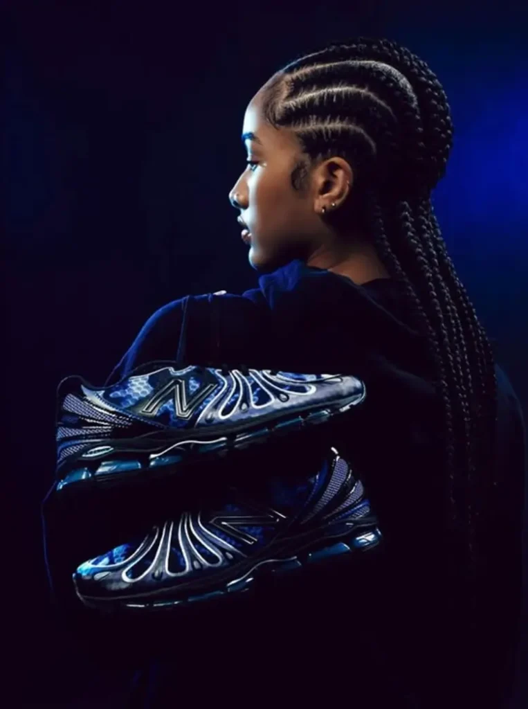 Woman with long braided hair in profile, holding blue and black New Balance sneakers against dark blue background
