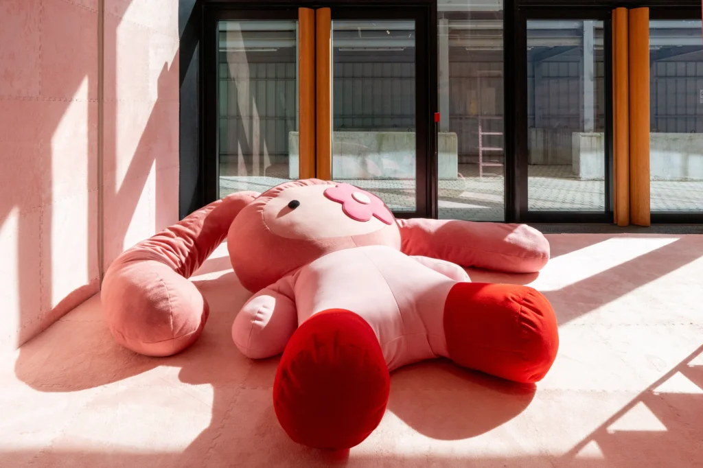 Oversized juju plush installation by Cj Hendry laid across a sunlit gallery floor, emphasizing scale, soft sculpture, and immersive exhibition design at Phillips Hong Kong