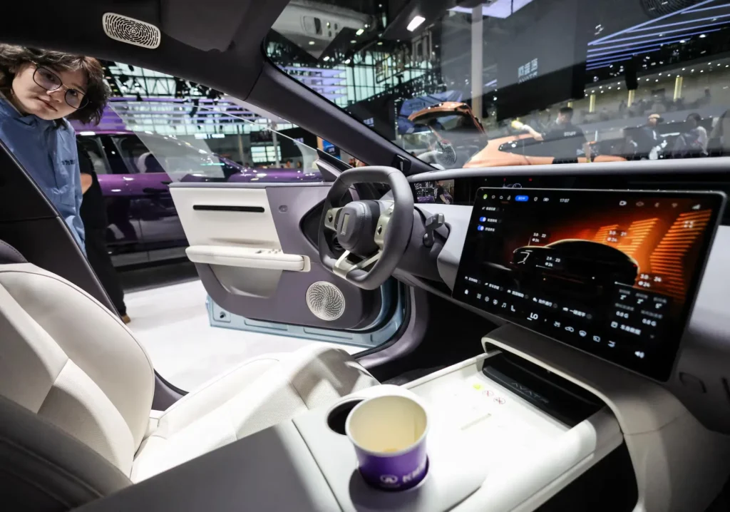 Interior view of a futuristic electric concept car at Auto China 2026, featuring a wide touchscreen interface with vehicle data visualization, minimalist steering wheel, light-colored cabin materials, and an attendee observing through the open doo
