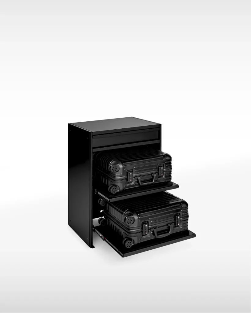 Minimalist black storage cabinet with two pull-out shelves, each holding a compact hard-shell suitcase, shown against a clean light background