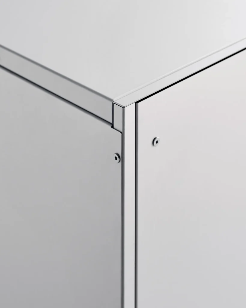 Close-up of a minimalist white metal cabinet corner, showing clean panel edges, a precise right-angle joint, and two small exposed screws on a smooth matte surface