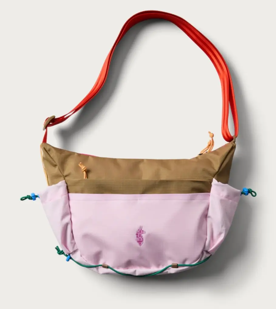 Color-blocked Cotopaxi x Free People shoulder bag in ginger khaki and powder pink, featuring a bright red adjustable strap, green cord detailing, and a small embroidered logo centered on the front panel