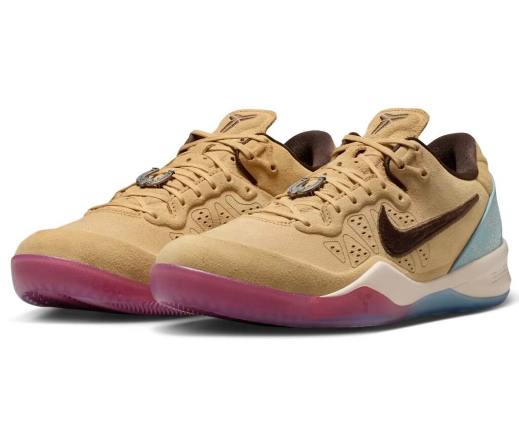 Three-quarter view of a pair of Nike basketball shoe in a tan suede finish, featuring dark brown Swooshes, tonal laces, and perforated side panels. The shoes include a metallic horseshoe-shaped lace charm and Kobe logos on the tongues, set atop a cream midsole with a translucent gradient outsole that shifts from pink at the forefoot to icy blue at the heel, with a textured turquoise heel overlay adding contrast