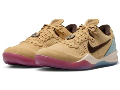 Three-quarter view of a pair of Nike basketball shoe in a tan suede finish, featuring dark brown Swooshes, tonal laces, and perforated side panels. The shoes include a metallic horseshoe-shaped lace charm and Kobe logos on the tongues, set atop a cream midsole with a translucent gradient outsole that shifts from pink at the forefoot to icy blue at the heel, with a textured turquoise heel overlay adding contrast