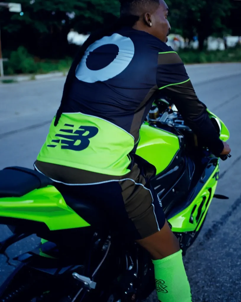 Person wearing black and neon green New Balance gear riding a bright green motorcycle on a road
