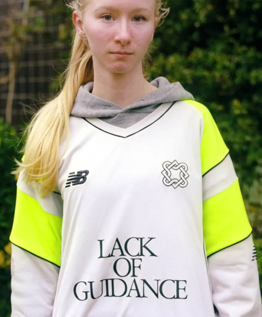 Young person wearing a grey and neon-accented “Lack of Guidance” jersey over a hoodie, standing outdoors