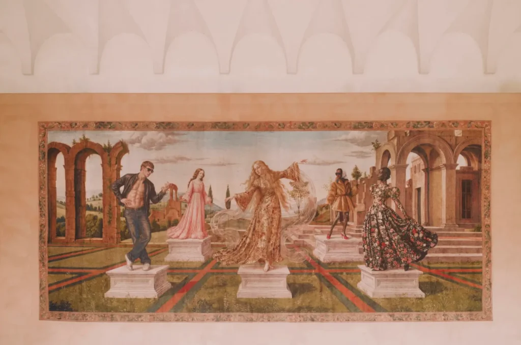 Large Renaissance-style mural featuring contemporary fashion figures posed on pedestals within a classical garden scene, blending historic architecture with modern styling beneath a vaulted ceiling