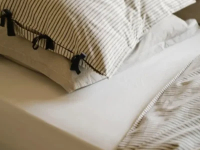 Cozy bed styled with Rowan Print Bedding, showing soft beige and black fine-striped pillowcases with elegant black tie closures on the envelope opening. The pillows rest on crisp white sheets alongside a matching striped duvet, creating a calm, timeless, and textured neutral bedroom scene