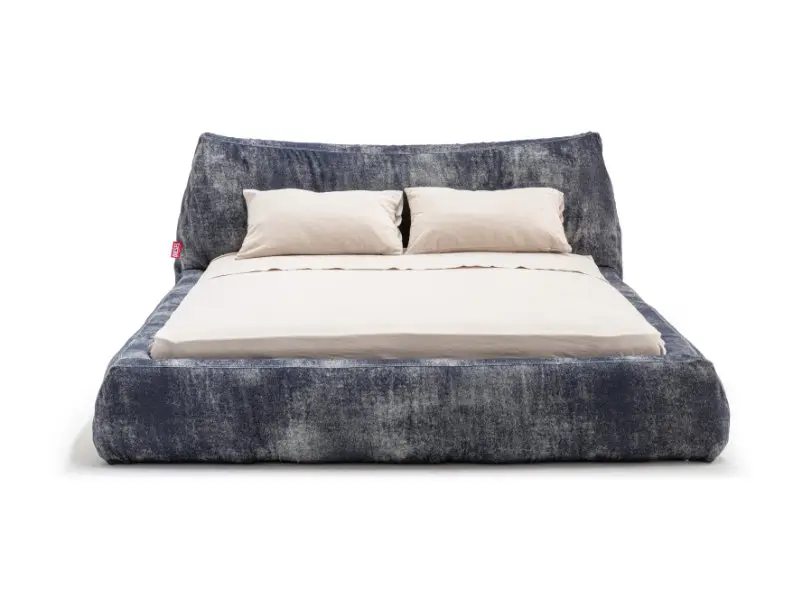 Diesel Living with Moroso Baggy Bed featuring a low, oversized silhouette with soft, rounded edges and a relaxed, denim-textured upholstery, paired with neutral bedding and pillows, emphasizing comfort, volume, and the translation of Diesel’s casual aesthetic into contemporary furniture design