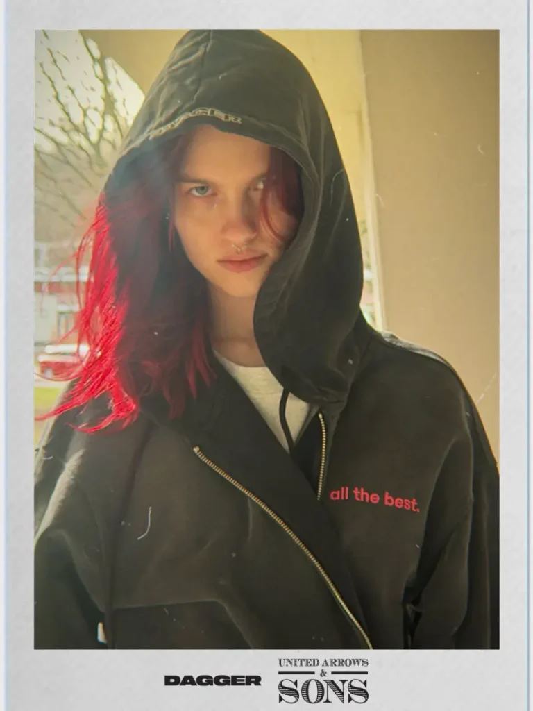 DAGGER x United Arrows & Sons campaign close-up featuring a model in a black zip hoodie with red “all the best” text, highlighted by soft natural light and a warm, cinematic streetwear tone