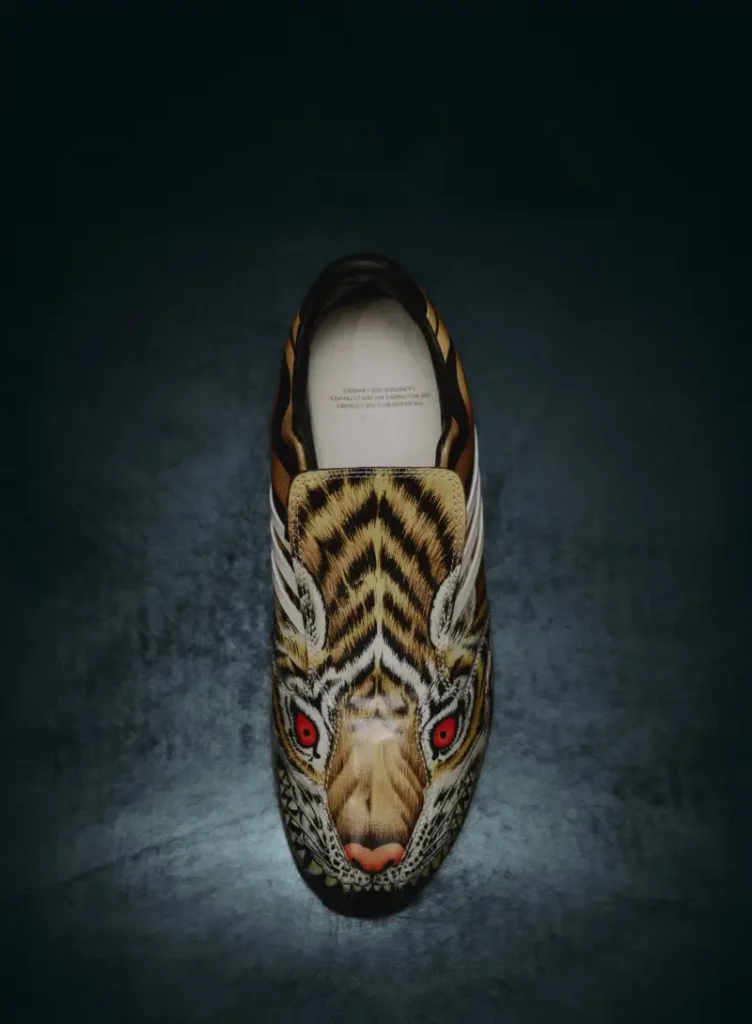 Top-down view of a yellow Y-3 F50 TUNIT shoe featuring a tiger-inspired graphic with bold stripes and red eyes, set against a dark textured background
