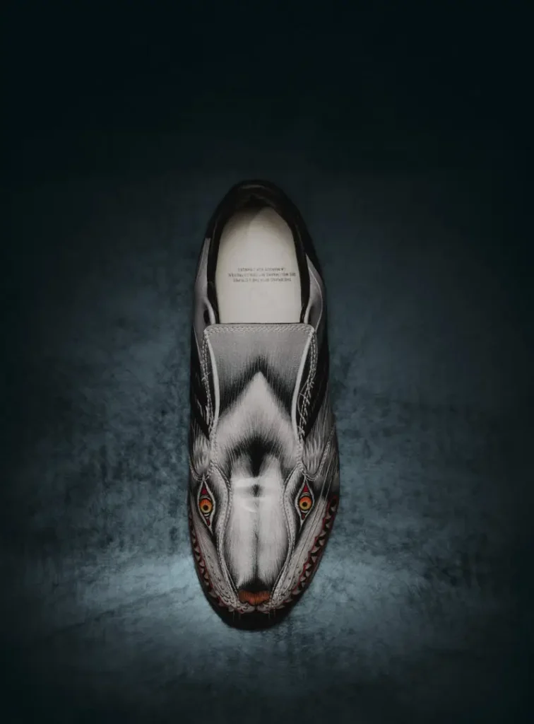 Side profile of a black and silver Y-3 F50 TUNIT football boot with wolf-inspired graphics, fold-over tongue, and black adidas stripes on a dark reflective studio surface