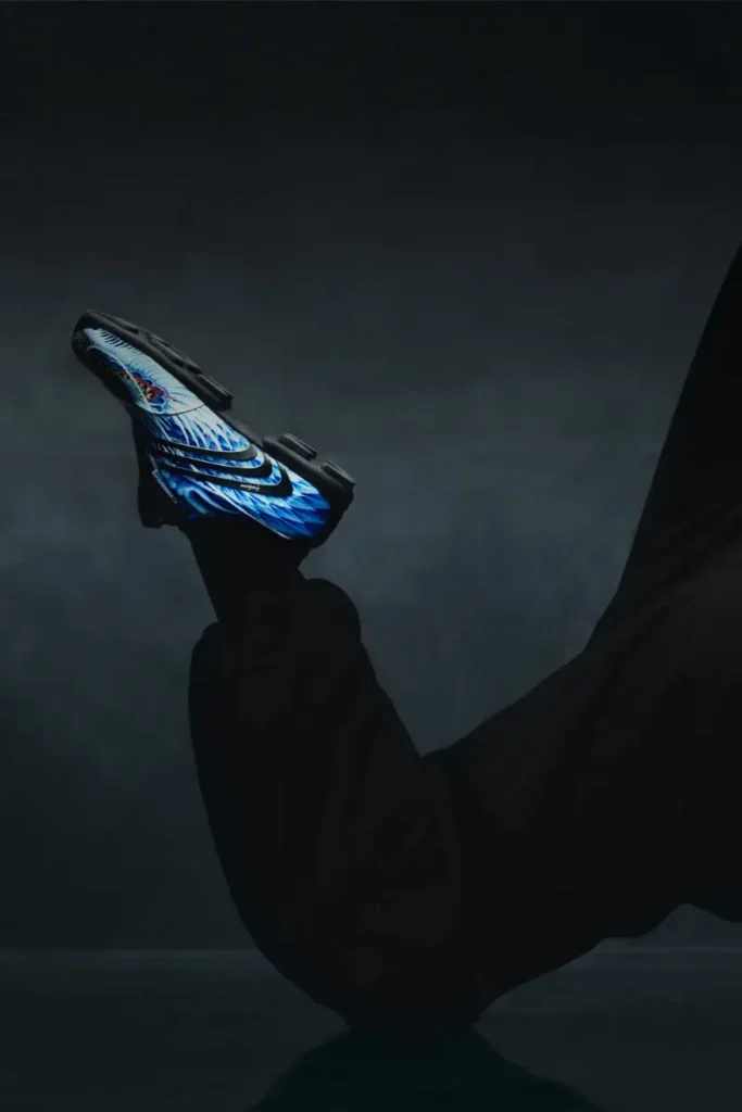 Blue Y-3 F50 TUNIT football boot with dragon graphic balanced on a foot in a dark, moody studio setting