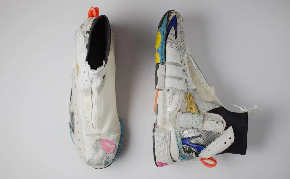 Top and side view of a deconstructed white shoe featuring exposed foam, cutaway panels, mixed materials, colorful accents, and visible stitching, emphasizing an experimental, inside-out design
