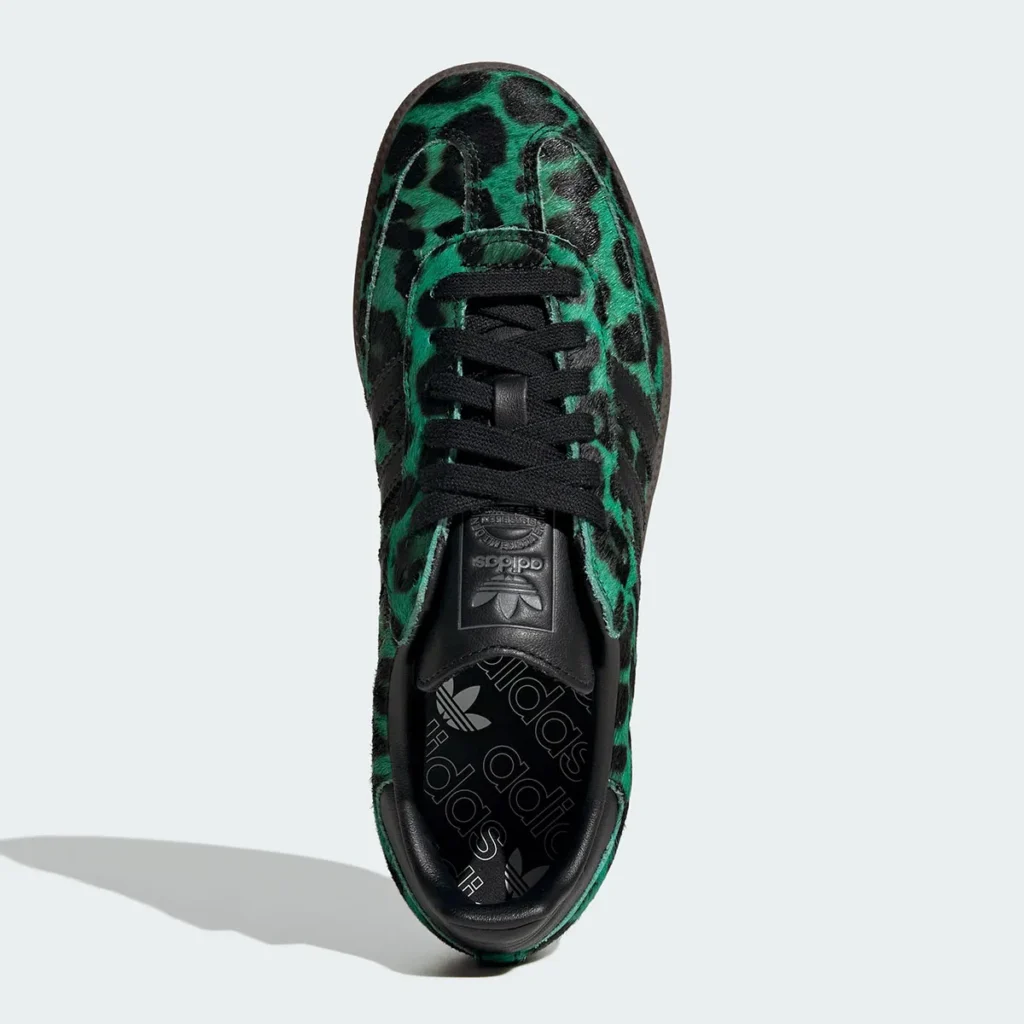 Top-down view of a low-profile shoe featuring a green-and-black leopard print pony hair upper. The shoe includes black laces, a black leather tongue with embossed adidas Trefoil branding, and a padded black collar. The interior footbed displays repeated adidas logos, while the textured material and bold pattern define the shoe’s standout design