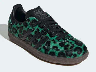 Three-quarter front view of a low-profile shoe featuring a green-and-black leopard print pony hair upper. The shoe is detailed with black laces, a black leather tongue with embossed adidas Trefoil logo, and matching black three-stripe overlays along the side. A dark gum sole grounds the design, while visible stitching and textured materials emphasize its elevated, fashion-forward construction