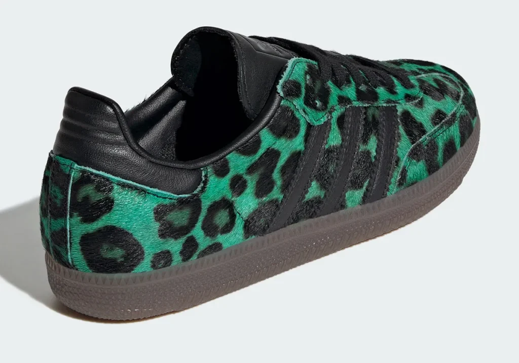 Rear three-quarter view of a low-profile shoe featuring a green-and-black leopard print pony hair upper. The design includes black leather heel tab and collar, tonal black three-stripe overlays along the side, and a semi-translucent gum sole. The textured surface and contrast between materials highlight a bold, fashion-forward take on a classic silhouette