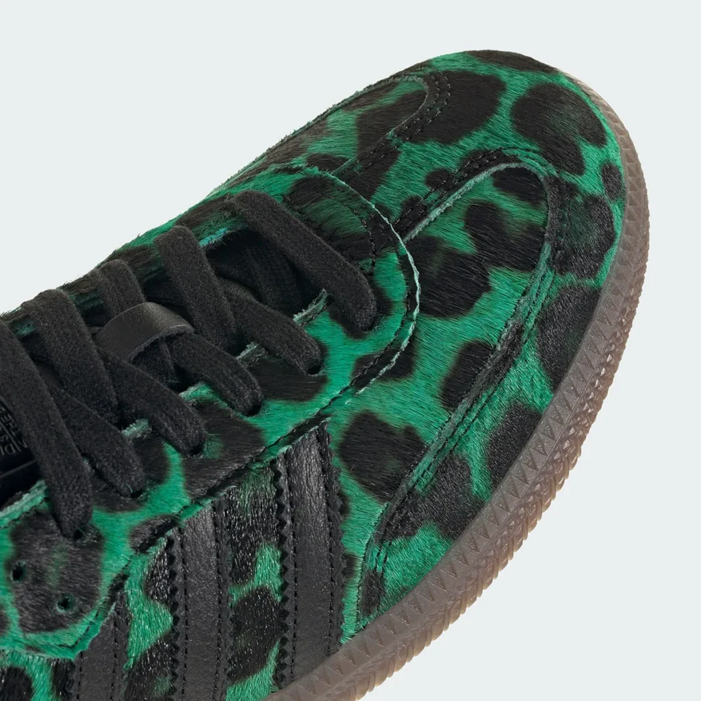 Close-up of a low-profile shoe featuring a textured pony hair upper in a bold green-and-black leopard print. The shoe includes black laces, black leather overlays forming the signature three stripes, and a translucent gum sole. Fine stitching details and the tactile surface emphasize the premium, fashion-forward finish of the design