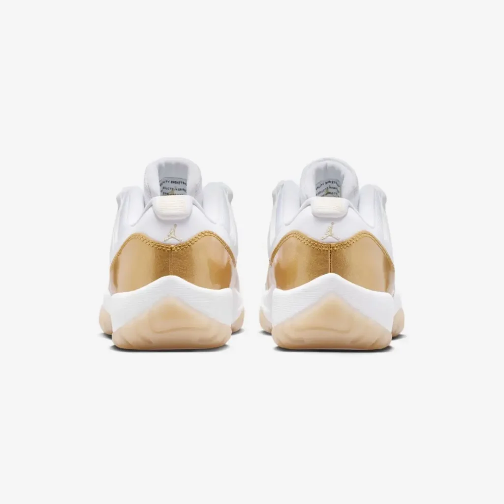 Rear view of a pair of white low-top shoe with metallic gold patent leather heel wraps, featuring small gold Jumpman logos on the back tabs, white midsoles, and translucent gum outsoles, displayed symmetrically against a neutral background